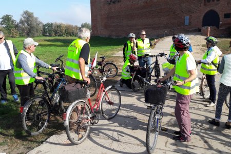 Grupka rowerzystów w odblaskowych kamizelkach przed wejściem na dziedziniec Zamku Książąt Mazowieckich