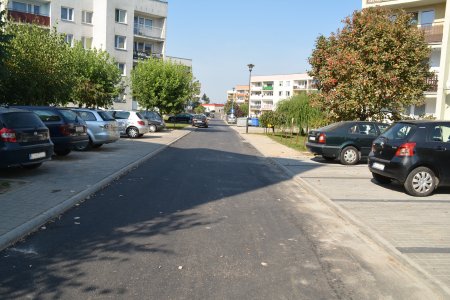 Ulica Bojanowskiego. Po obu stronach miejsca parkingowe i parkujące auta. Po obu stronach ulicy bloki