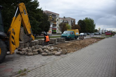 Koparka zrywa starą nawierzchnię z trylinki z pasa, o który zostanie poszerzony parking. W oddali widać bloki