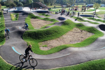 Pofalowane alejki pumptracku. Między nimi trawniki. Na pierwszym planie jadący rowerzysta