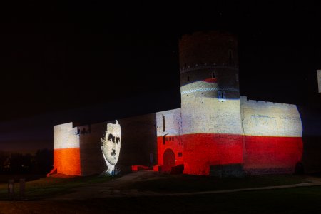 Zamek Książąt Mazowieckich po zmierzchu. Podświetlony narodowymi barwami. Na ścianie od strony ul. Zamkowej wyświetlona podobizna Romana Dmowskiego