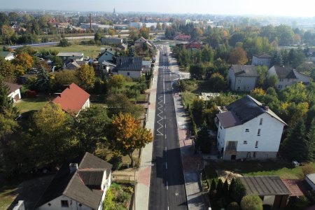 Ulica Kwiatowa z wysoka. Przecina kadr zdjęcia na pół. Widać linie namalowane na jezdni. Op obu stronach ulicy domy i dużo zieleni