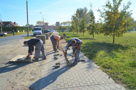 Trzech pracowników demontuje nawierzchnię chodnika. Brukową kostkę układają na palecie.