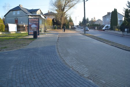 Nowa zatoka autobusowa. Chodnik dla pasażerów i podjazd dla autobusów wykonano z brukowej kostki. Pośrodku chodnika stoi nowa zadaszona i oszklona wiata z ławką dla oczekujących