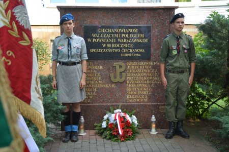 Warta harcerska przy pomniku poświęconym ciechanowianom walczącym i poległym w powstaniu warszawskim. Pod pomnikiem leży wieniec. Po lewej widać fragment sztandaru z orłem