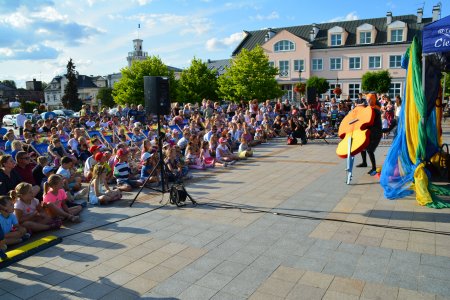 Plac Jana Pawła II. Po lewej bardzo liczna publiczność. Po prawej aktor teatralny z wielkim kontrabasem odwróconym do góry nogami. Najbardziej po prawej widać fragment namiotu należącego do Urzędu Miasta i zawieszone na nim tkaniny