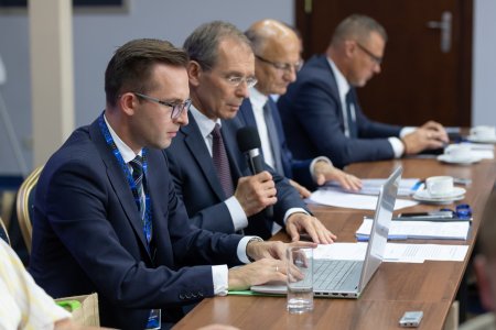 Obradujący samorządowcy siedzą za stołem. Na pierwszym planie prezydent Ciechanowa, który ma przed sobą laptop. Na stole leżą porozkładane dokumenty