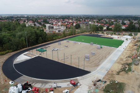 Ogromne boisko widziane z góry. Obiekt nie jest wykończony. Pośrodku trwa budowa nawierzchni. Na zewnątrz wykopy i materiały budowlane