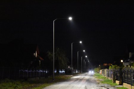 Rząd świecących lamp ulicznych wzdłuż drogi. Po prawej widać ogrodzenia posesji