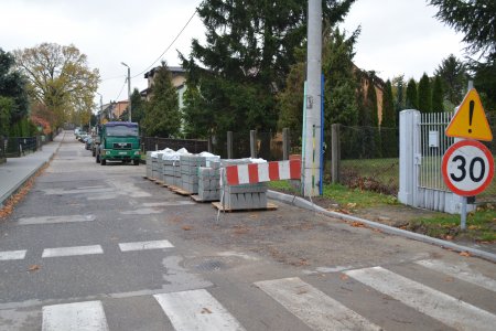 Ulica Borodzicza. Po obu stronach posesje. Tuż za przejściem dla pieszych stoi znak ograniczenia prędkości do 30 km/h. Po prawej stronie ulicy ustawiono rząd palet z krawężnikami, dalej stoi ciężarówka, a za nią zaparkowane auta.