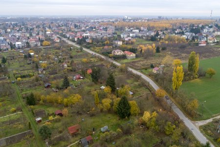 Zdjęcie wykonane z wysoka. Ulica Leśna przecina kadr na skos . W dolnej części zdjęcia niewiele zabudowań i dużo zieleni. W górnej części osiedle domów jednorodzinnych z gęstą zabudową