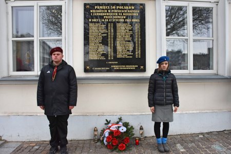 Tablica na ratuszu, na której zapisano nazwiska osób zamordowanych przez hitlerowców tuż przed 17 stycznia. Po obu stronach tablicy stoi watra. Pod tablicą złożono kwiaty