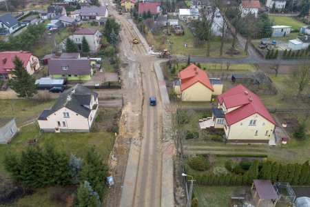 Ulica pokazana z wysoka. W górnej części pokazanego odcinka rozpoczęły się roboty. Na środku jezdni pracuje maszyna drogowa. Po obu stronach drogi są prywatne posesje z domami jednorodzinnymi.