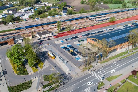 Zdjęcie zrobione z wysoka. W kadrze po lewej mieści się budynek dworca kolejowego, niżej znajduje się skwer z fontanną, Dalej w prawo jest parking, a po prawej stronie zdjęcia jest Hala Targowa. Powyżej, wzdłuż całej hali, ciągną się dwa rzędy miejsc parkingowych. Na górze, przez całą szerokość fotografii biegną tory kolejowe z rampą do przeładunku towarów. 