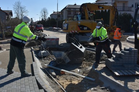 Trwa przebudowa ulicy. Pracownicy drogowi oprócz odblaskowych ubrań ochronnych, mają na twarzach maseczki.