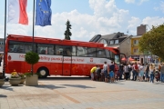 Na placu Jana Pawła II stoi oznakowany autokar - mobilny punkt  poboru krwi. Przed przednimi drzwiami autokaru stoi kolejka chętnych do oddania krwi. Obok, przy stoliku kolejni chętni wypełniają ankiety