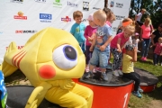 Kilkoro maluchów stoi lub siedzi na najwyższym stopniu podium. Obok siedzi człowiek przebrany za rybę z wielkimi oczami