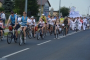 Parada ulicami miasta. Na pierwszym planie rowerzyści w różnym wieku, dalej idą dzieci i młodzież z klubu pływackiego, niosący transparent z napisem 