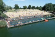 Zdjęcie wykonane z wysokości. Na zdjęciu kąpielisko Krubin - fragment zbiornika wodnego z pomostem i plażą. Na plaży plażowicze. Przy pomoście zacumowana łódka