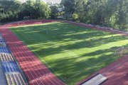 Miejski stadion, zdjęcie zrobione z lotu ptaka. Na murawę stadionu długie cienie rzucają stare, wysokie drzewa rosnące po prawej