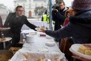 Prezydent podaje kobiecie talerz z kapustą i pierogiem. Filmuje to mężczyzna z kamerą.