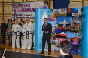 Prezydent Ciechanowa przy mirofonie stoi na tle ścianki promującej Ciechanów. Po jego prawej stronie grupa trenerów taekwon-do w dobokach (ubrania treningowe)