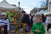 Po prawej i lewej stronie deptaku rzędy stoisk. Między nimi wielu spacerujących ludzi. Po lewej stojak ze świątecznymi stroikami