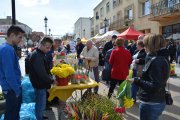 Stoisko z kwiatami. Na pierwszym planie kobieta z bukietem kwiatów w ręku. Przy stoisku mężczyzna z portfelem w ręku patrzy na kwiaty na stoliku