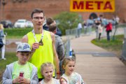 Po ukończeniu biegu na mecie przy Zamku Książąt Mazowieckich mężczyzna prezentuje swój medal. Przed zawodnikiem stoi trójka dzieci