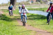 Wydeptaną ścieżką wzdłuż rzeki jedzie na rowerach pięcioro zawodników w różnym wieku