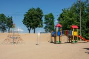 Kolorowy plac zabaw dla dzieci na plaży kąpieliska Krubin. Po lewej są liny do wspinania, po prawej drabina, zjeżdżalnia, tunel, dwie wieże pod daszkami.