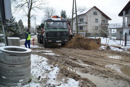 Ul. Bielińska, wywrotka przywiozła żwir na podbudowę ulicy. Po lewej leżą okrągłe betonowe elementy konstrukcyjne 