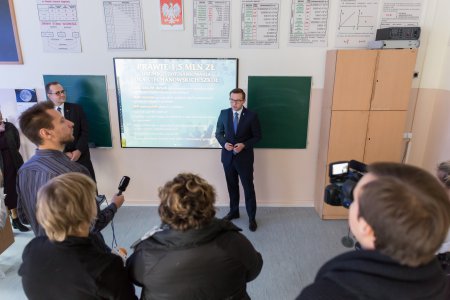 Konferencja prasowa Miejskim Zespole Szkół Nr 1. Prezydent Ciechanowa, stojąc przy szkolnej tablicy odpowiada na pytania dziennikarzy. 