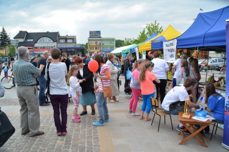 Zdjęcie wykonane podczas festiwalu wolontariatu, który odbył się latem. Na pl. Jana Pawła II stoją namioty, w których prezentują się organizacje pozarządowe. Dorośli i dzieci spacerują i oglądają prezentacje.