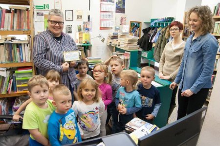 Zajęcia w miejskiej bibliotece. Grupka małych dzieci i panie bibliotekarki