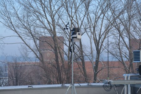 Zdjęcie z dachu ratusza. Na zdjęciu czujnik stacji pogodowej, znajdujący się na dachu ratusza. W tle, za rzędem drzew widać Zamek Książąt Mazowieckich w zimowej szacie