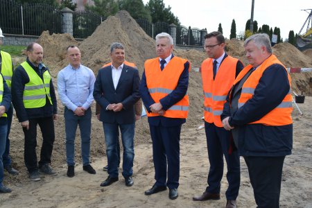 Uczestnicy konferencji prasowej na placu budowy ulicy Sońskiej. Za plecami stojących rzędem mężczyzn widać hałdy żwiru