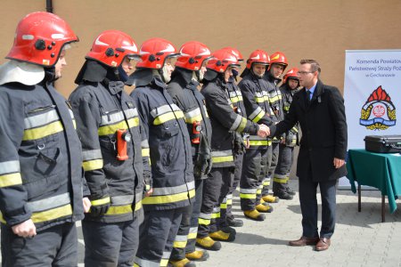 Po lewej rząd strażaków pełnym umundurowaniu. Prezydent Ciechanowa podaje rękę kolejnemu ze strażaków