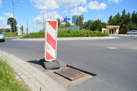 Słupek ostrzegawczy ustawion przed studzienką kanalizacyjną, wokół której wycięto asfalt