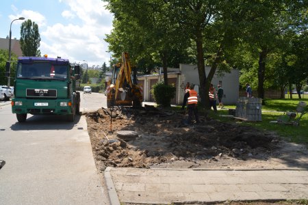 Trwa remont nawierzchni parkingu. Zdjęto starą nawierzchnię. Robotnicy wyrównują teren pod położenie nowej. Po lewej stoi samochód ciężarowy a za modernizowanym placem koparka