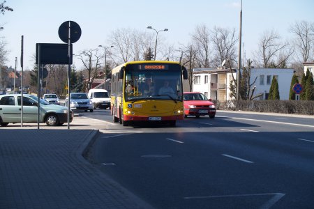 Ulicą 17 Stycznia jedzie autobus komunikacji miejskiej i wiele osobowych aut. Dzień jesienny ale słoneczny