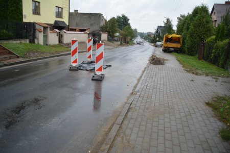 Pośrodku jezdni niewielki fragment jezdni przykryty czarną folią i zabezpieczony z trzech stron słypkami ostrzegawczymi