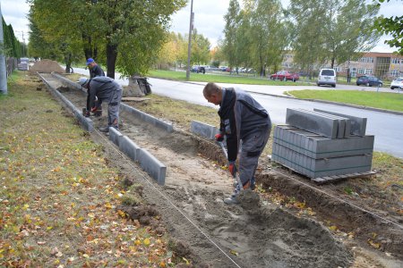 Robotnicy ustawiają nowe płyty krawężnikowe wzdłuż pasa gruntu, na którym powstanie chodnik