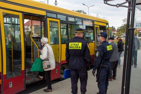 Do autobusu, który zatrzymał się na przystanku autobusowym, wsiadają pasażerowie. Stoją tu też dwaj strażnicy miejscy.. 