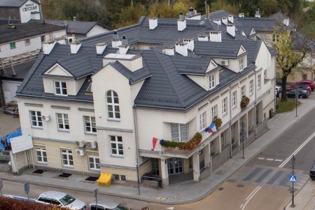 Zdjęcie wykonane z góry. W dole budynek Urzędy Miasta przy ulicy Wodnej. Dobrze widoczny jest szary łamany dach na budynku i wiele kominów.