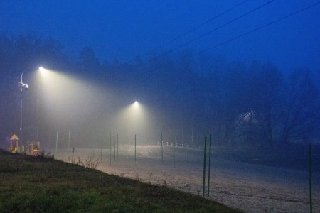 Zdjęcie zrobione po zmroku. Latarnie oświetlają plażę, plac zabaw dla dzieci oraz boisko do siatkówki plażowej.