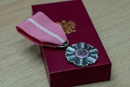 Medal z krótką, podwójnie złożoną szeroką tasiemką. Medal ma kształt kwiatu z płatkami. Na środku ma kółeczko, a w nim dwie rozwinięte róże połączone łodyżkami. Medal leży na ozdobnym pudełku ze złotym orłem pośrodku.