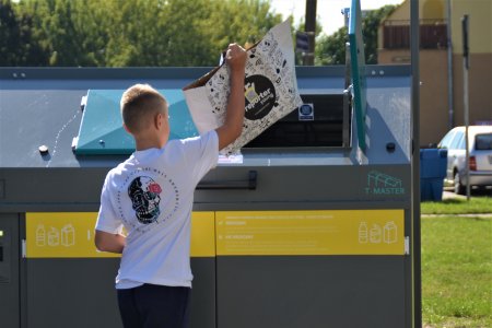 Chłopiec wrzuca papierową torbę do kontenera na papier.