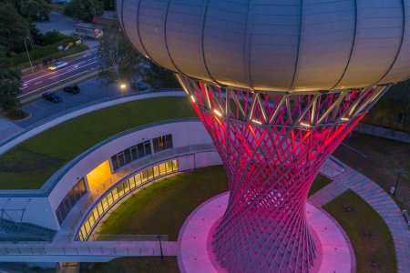 Wieża ciśnień i Park Nauki Torus widziane z góry. Podstawa wieży oświetlona na fioletowo. Wewnątrz parku nauki pali się światło.