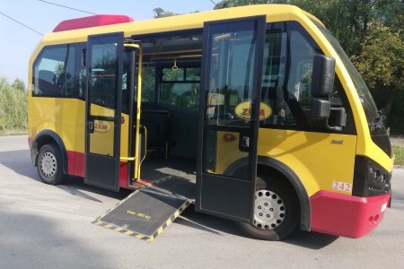 Miejski autobus z otwartymi drzwiami i wysuniętym podjazdem dla wózkowiczów i mam z wózkami dziecięcymi.